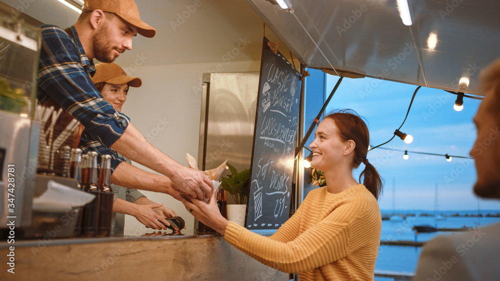 Food Truck Employee Hands Out a Freshly Made Burger to a Happy Young Female. Young Lady is Paying fo