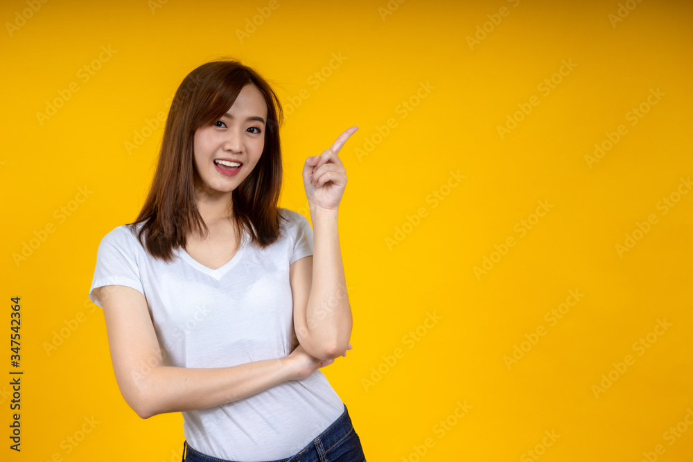 Young elegant Asian woman smiling and pointing to empty copy space isolated on yellow background