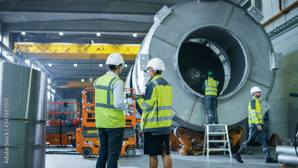 Two Heavy Industry Engineers Walk Through Pipe Manufacturing Factory, Use Digital Tablet Computer, H