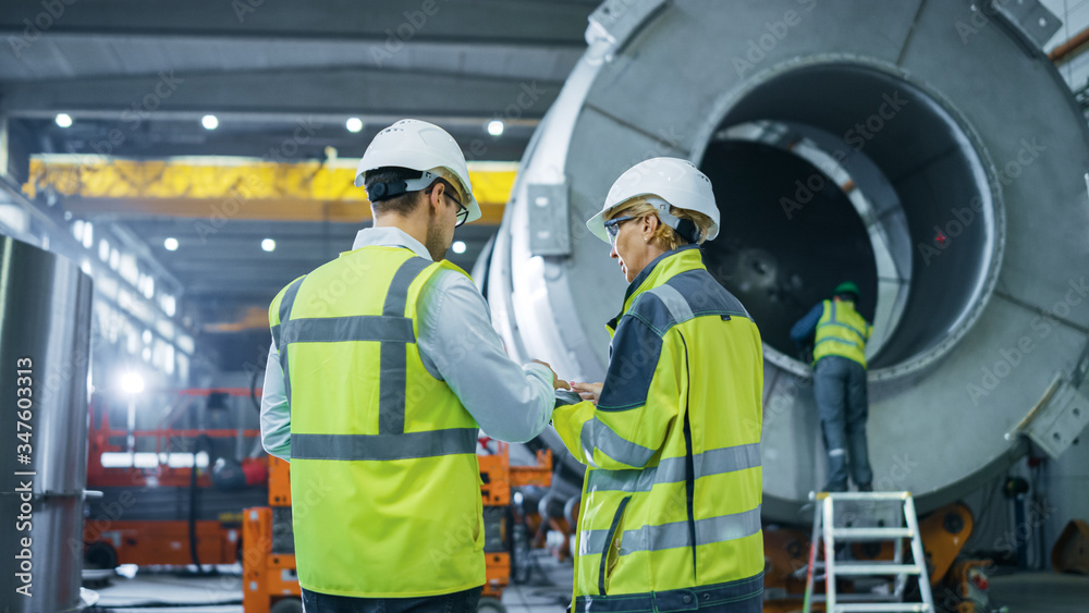 Two Heavy Industry Engineers Walk Through Pipe Manufacturing Factory, Use Digital Tablet Computer, H