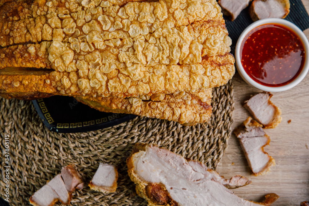 Large crispy pork on a black plate, cut into slices on a wooden chopping board with spicy sauce on a