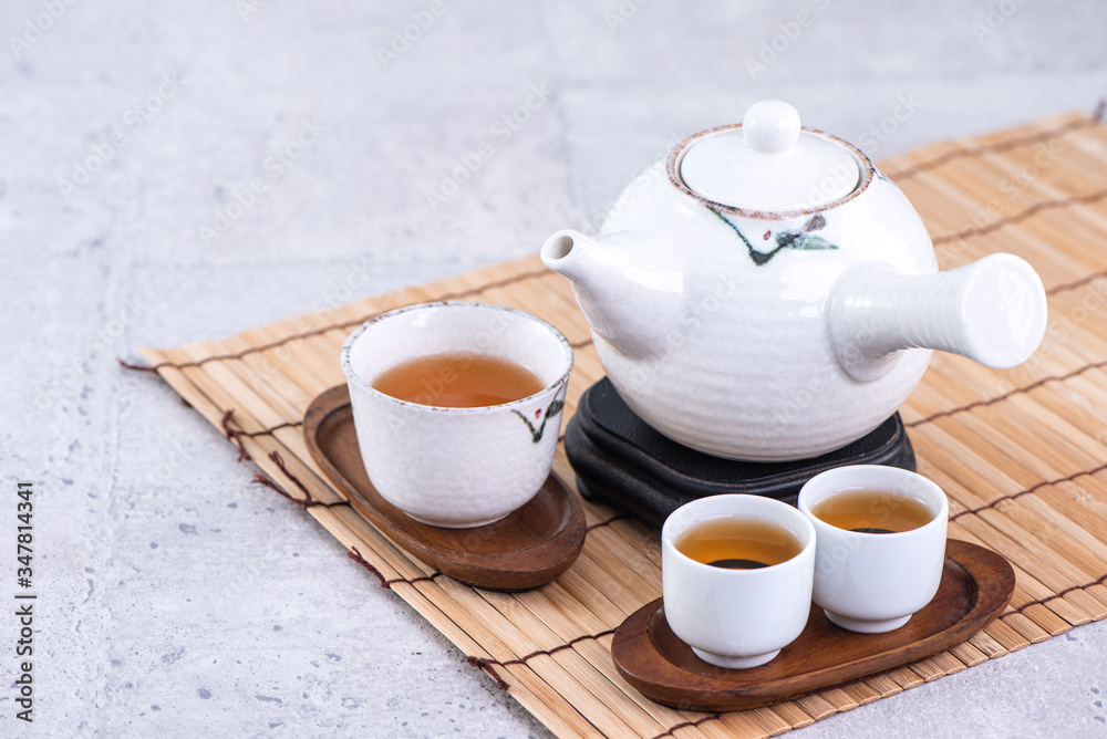 Hot tea in white teapot and cups on a sieve over bright gray cement background, closeup, copy space 