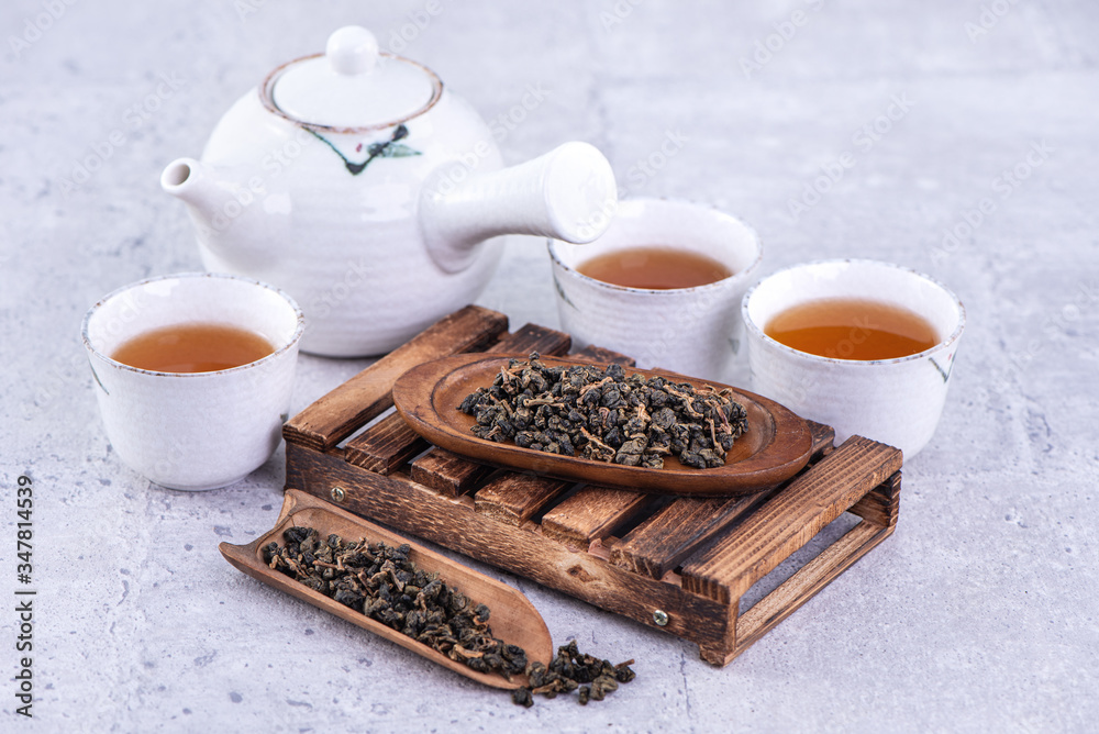 Hot tea in white teapot and cups on a sieve over bright gray cement background, closeup, copy space 