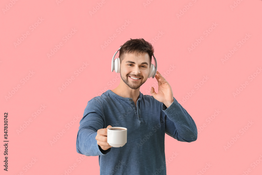 Young man with cup of hot coffee listening to music on color background