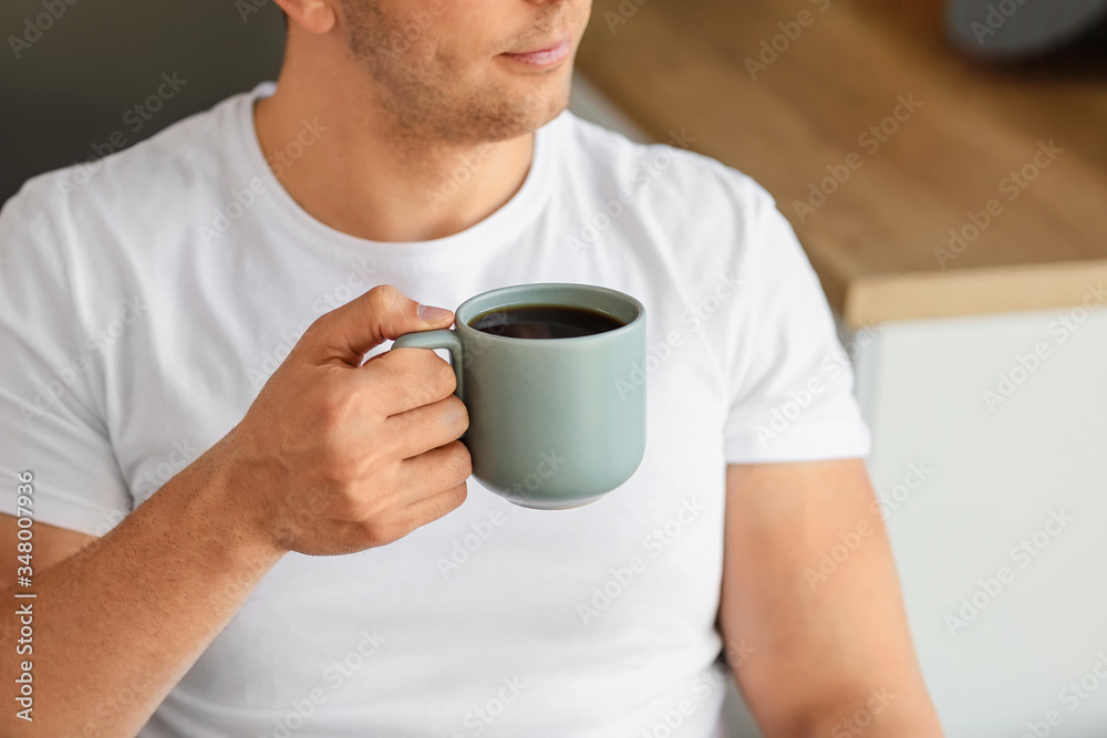 Handsome man drinking coffee in kitchen, closeup