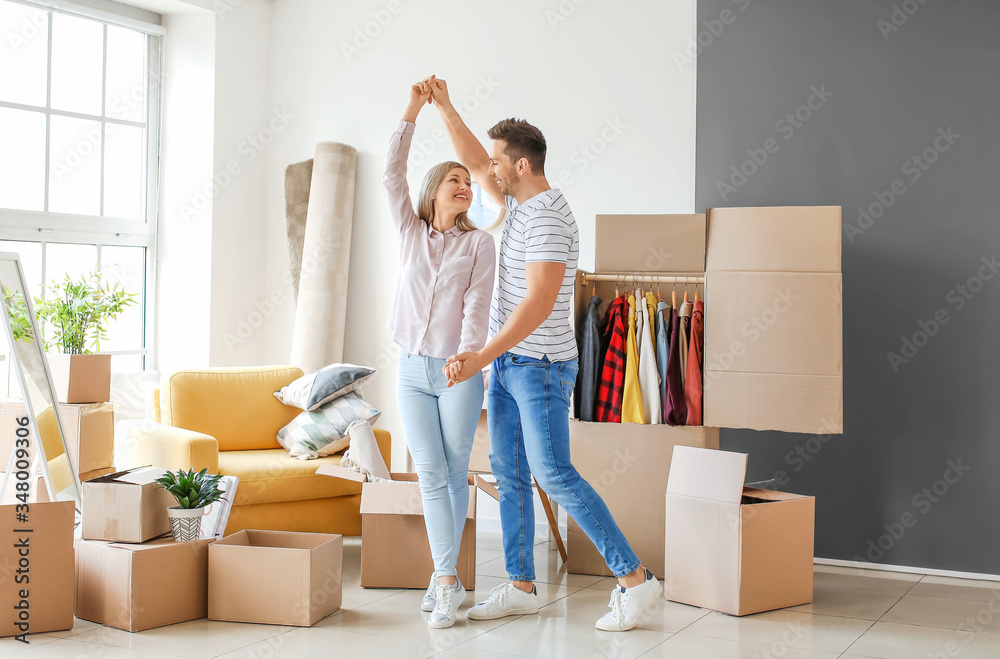 Young couple having fun while unpacking things in their new flat on moving day