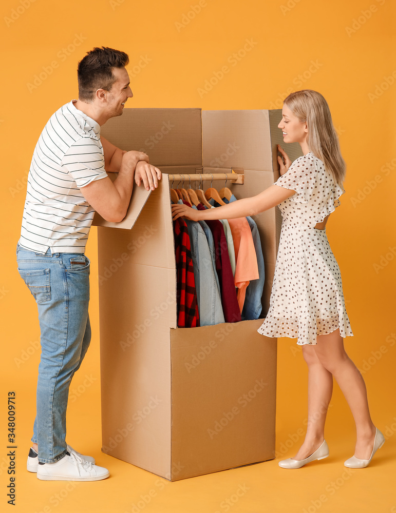 Young couple unpacking clothes on color background