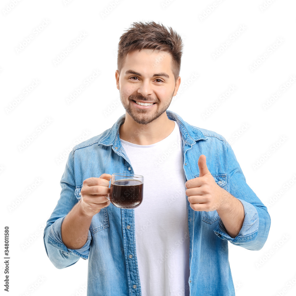 Young man with cup of hot coffee showing thumb-up on white background