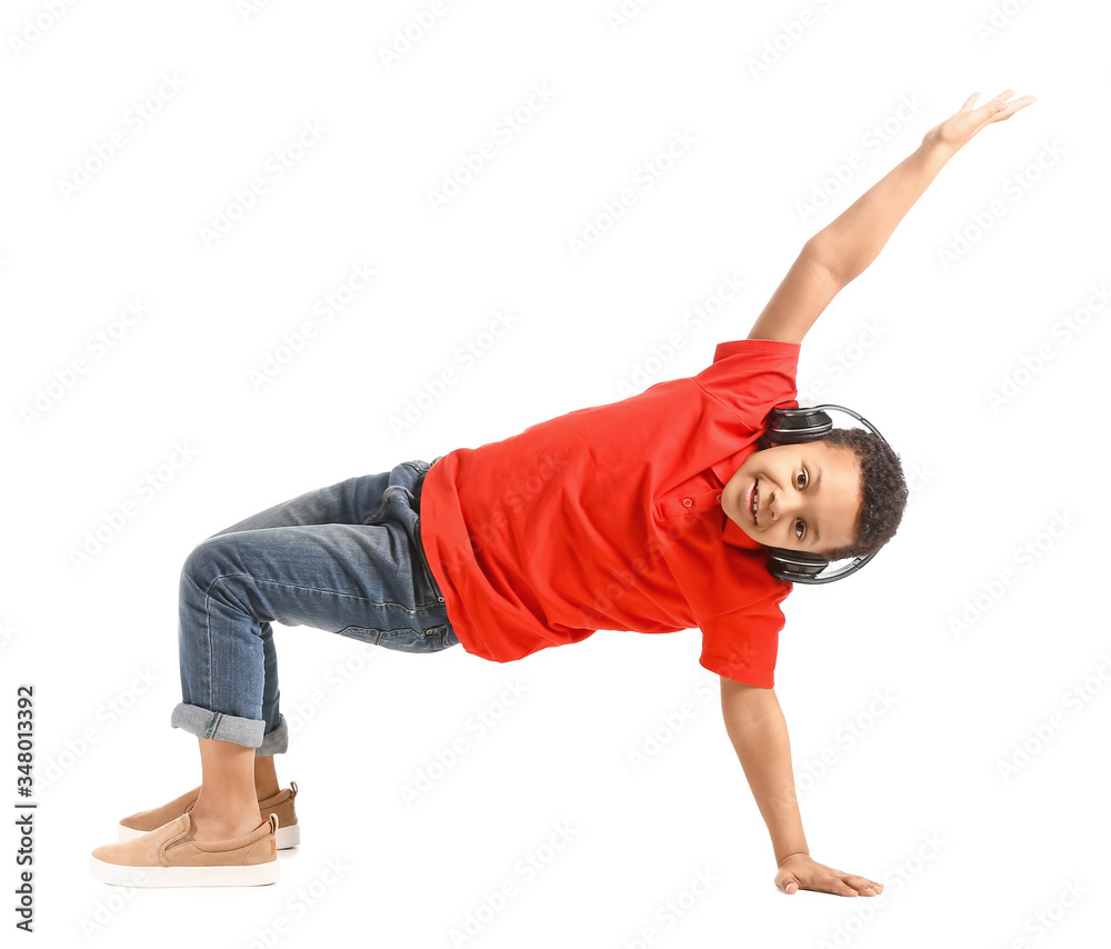 Little African-American boy listening to music and dancing against white background