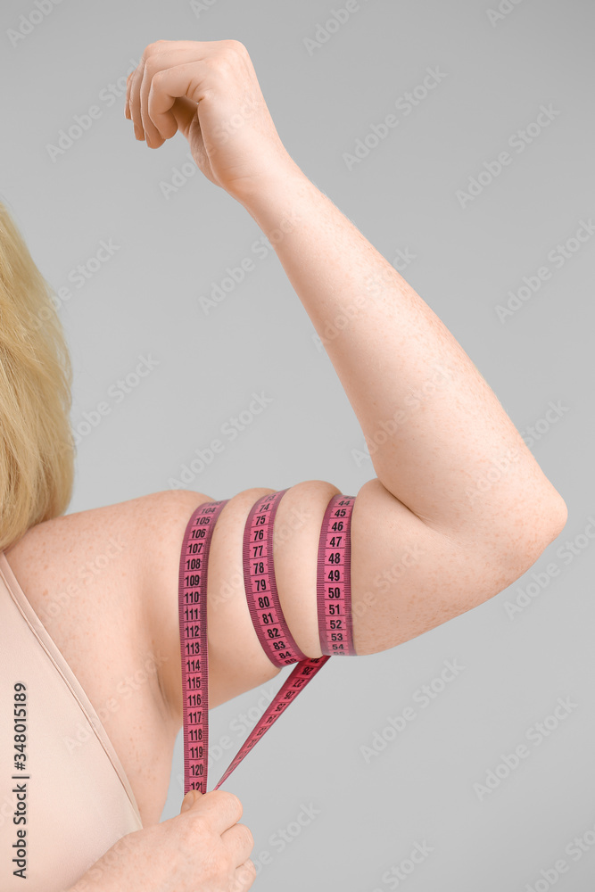 Overweight woman with measuring tape on grey background. Weight loss concept