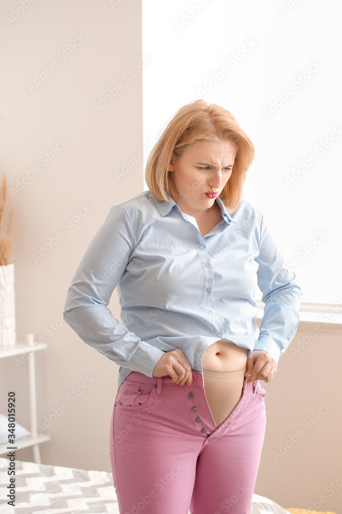 Displeased overweight woman in tight clothes at home. Weight loss concept