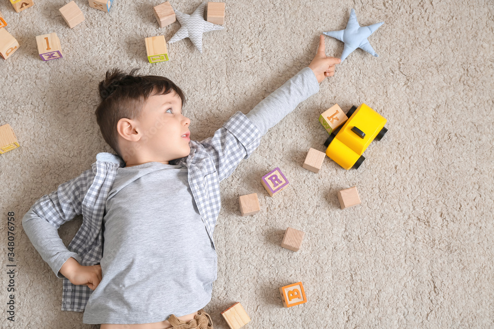 Little boy with toys lying on floor, top view