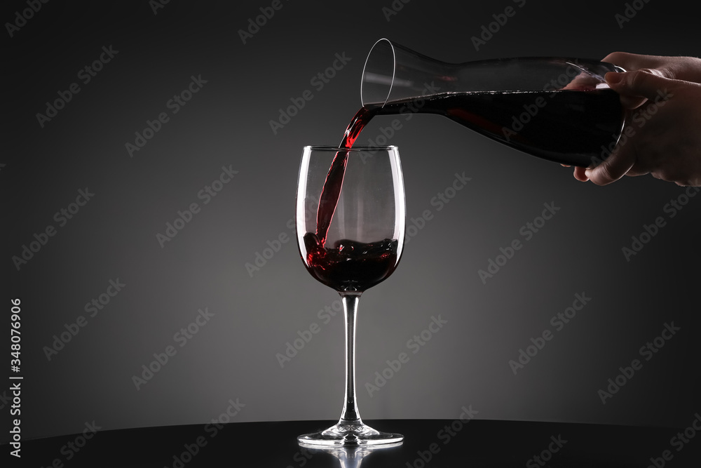 Pouring of tasty wine from decanter into glass on dark background