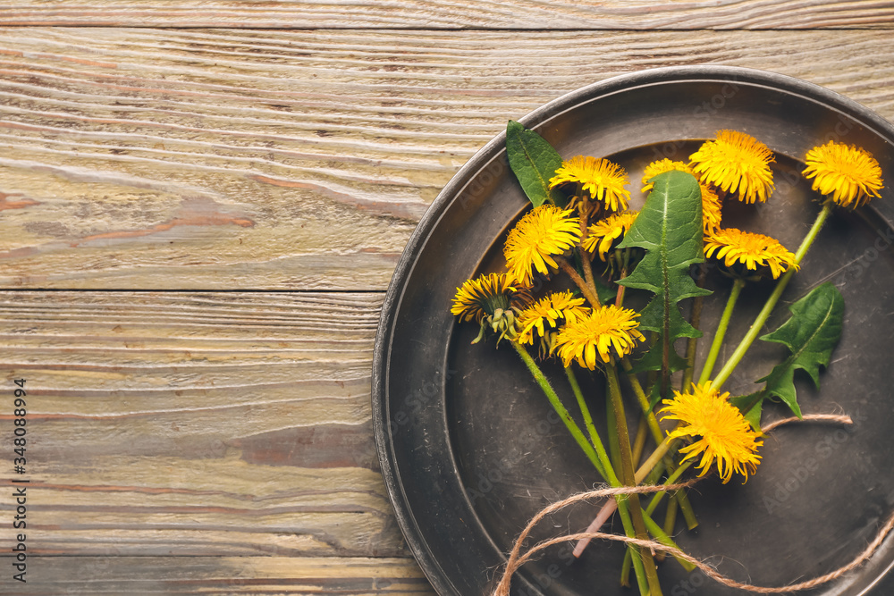 Plate with beautiful dandelions on wooden background