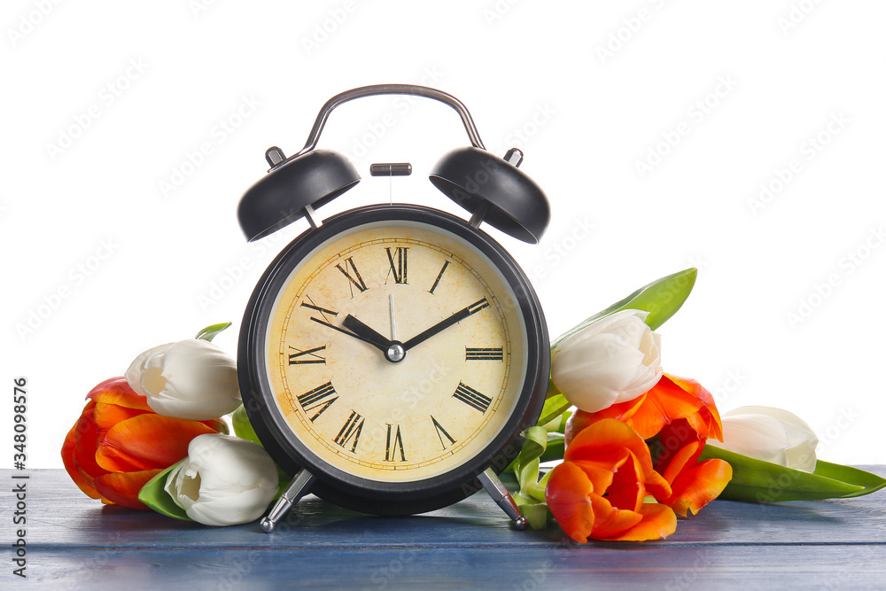 Alarm clock and flowers on table against white background. Spring time