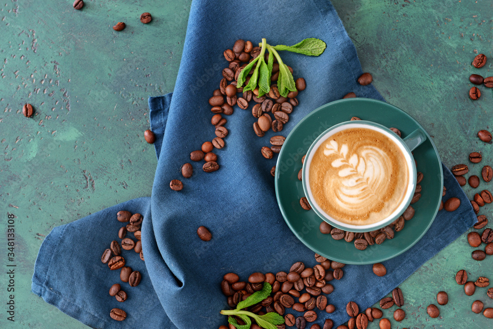 Cup of tasty cappuccino and coffee beans on color table