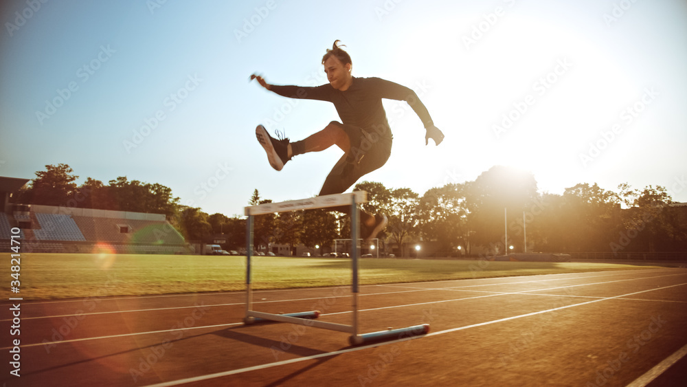 Athletic Fit Man in Grey Shirt and Shorts Hurdling in the Stadium. He is Jumping Over Barriers on a 