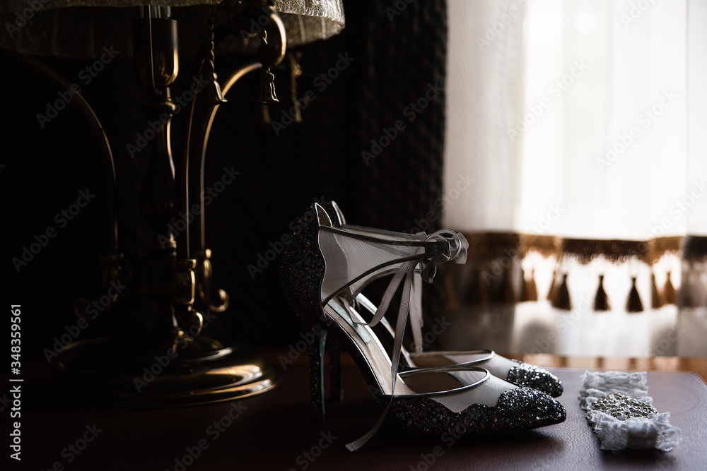 in a dark room by the window on the table are shoes, a floor lamp and a garter on the leg for the br