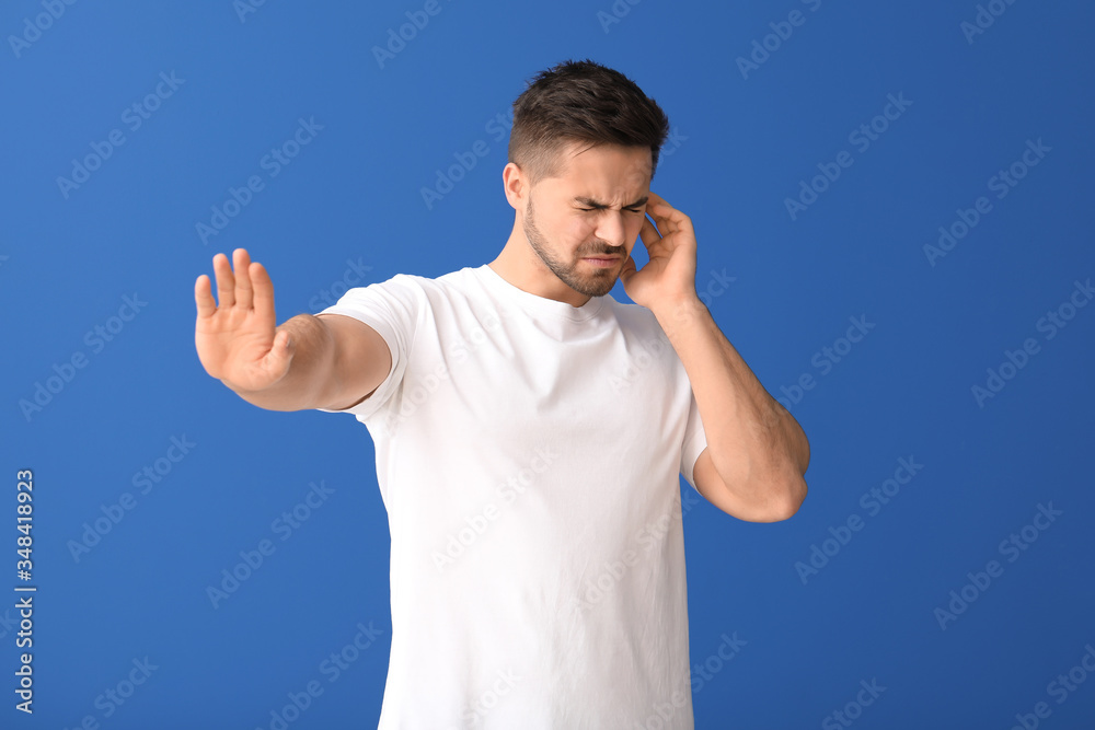 Young man suffering from loud noise on color background