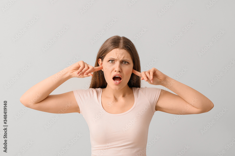 Young woman suffering from loud noise on light background