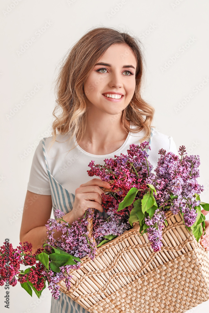 Beautiful young woman with bag and lilac flowers on white background