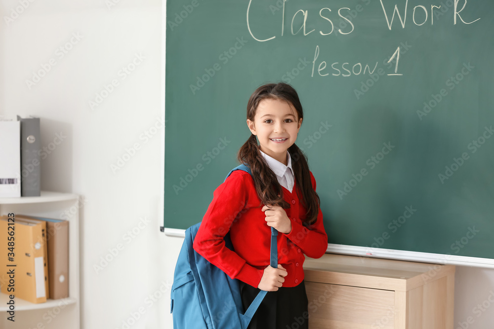 Cute little pupil near blackboard in classroom