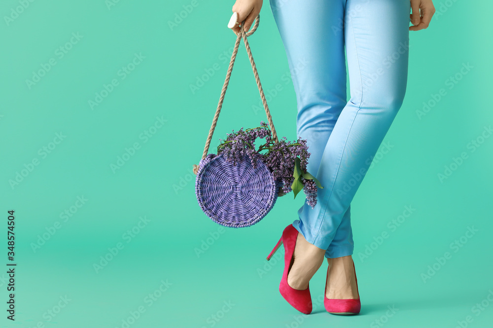 Beautiful young woman with lilac flowers and bag on color background