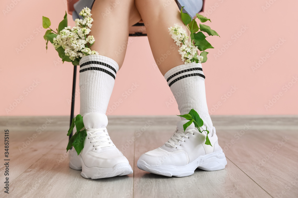 美丽的年轻女子，带着淡紫色的花朵，坐在靠近彩色墙的椅子上