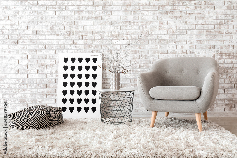 Comfortable armchair and table near brick wall