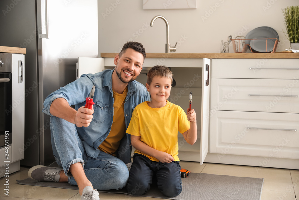 Little son helping his father to repair sink in kitchen