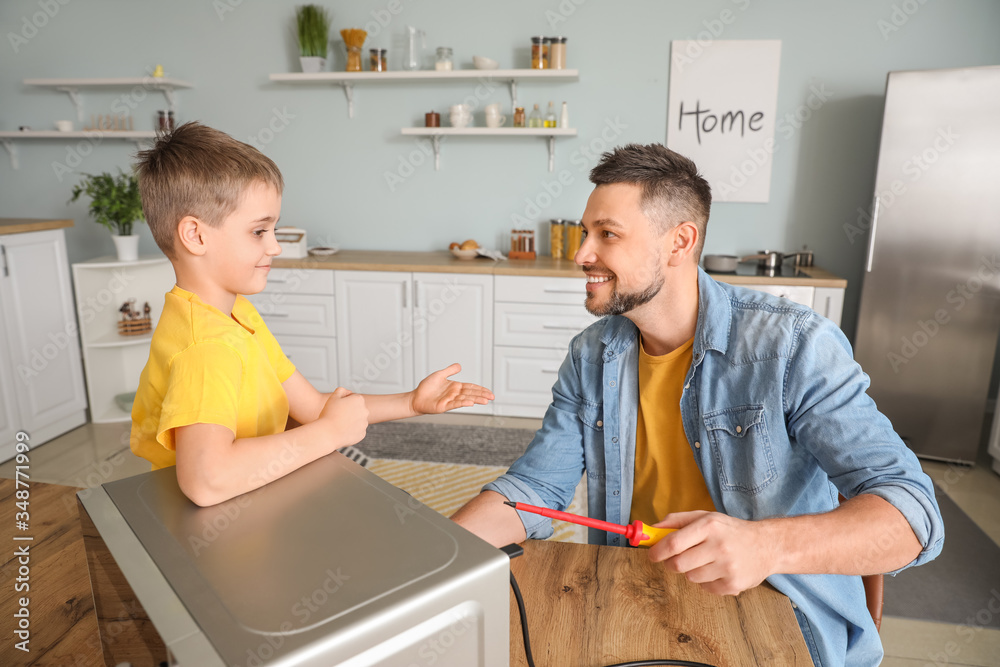 Little son helping his father to repair microwave oven in kitchen