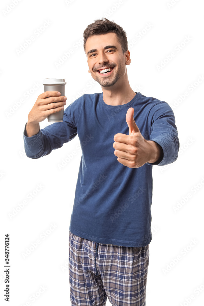 Young man with cup of hot coffee showing thumb-up on white background