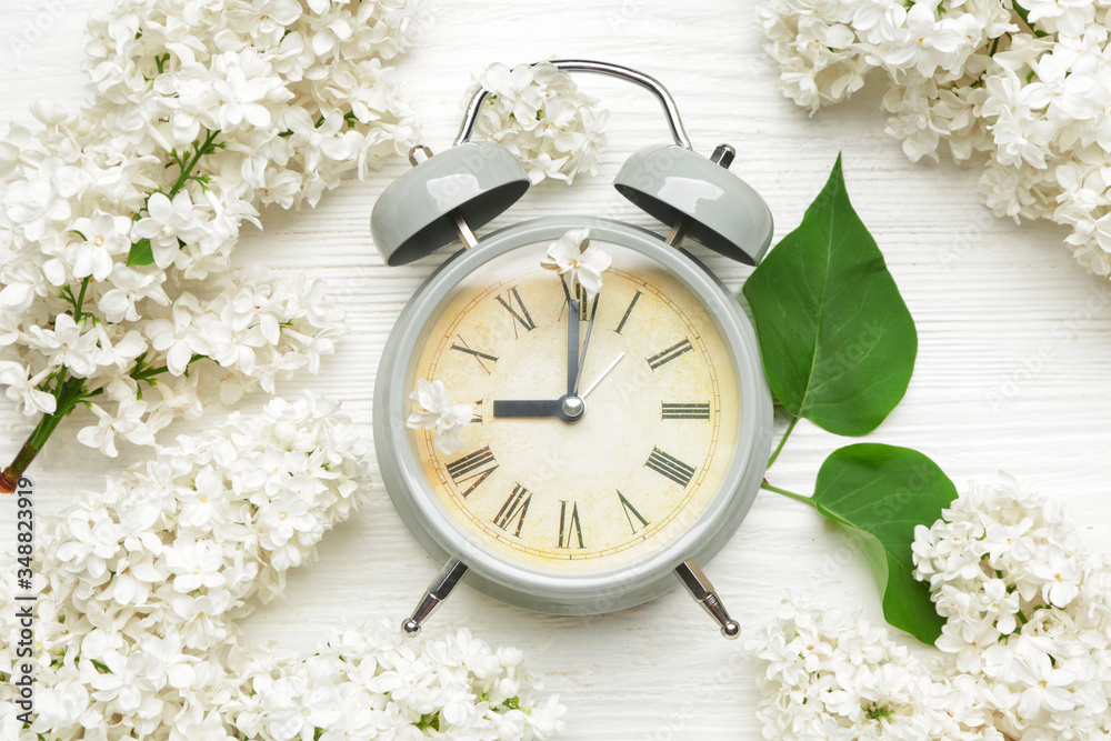 Alarm clock and flowers on white wooden background. Spring time