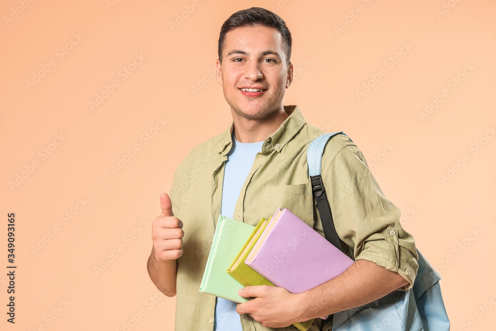 Portrait of male student showing thumb-up on color background