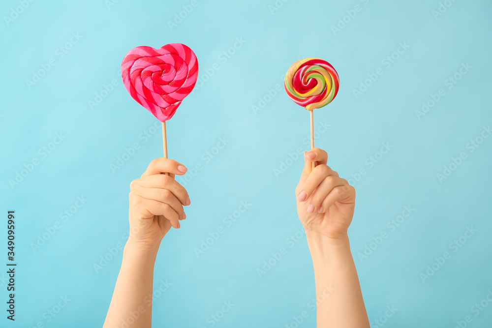 Hands with sweet lollipops on color background