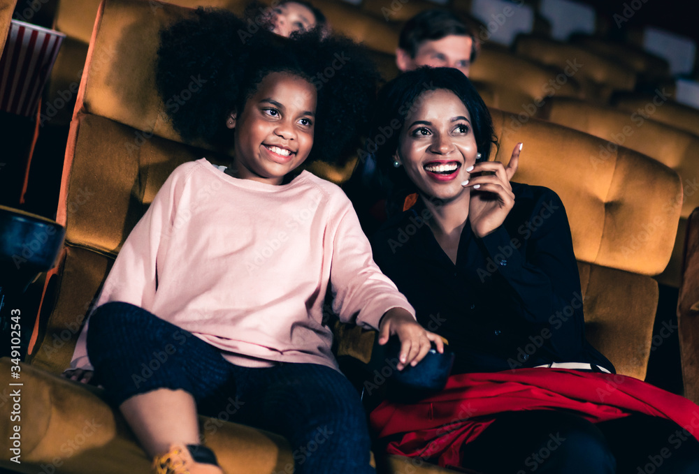 Woman enjoy to watch a movie with her daughter at the cinema smiling and laughing together