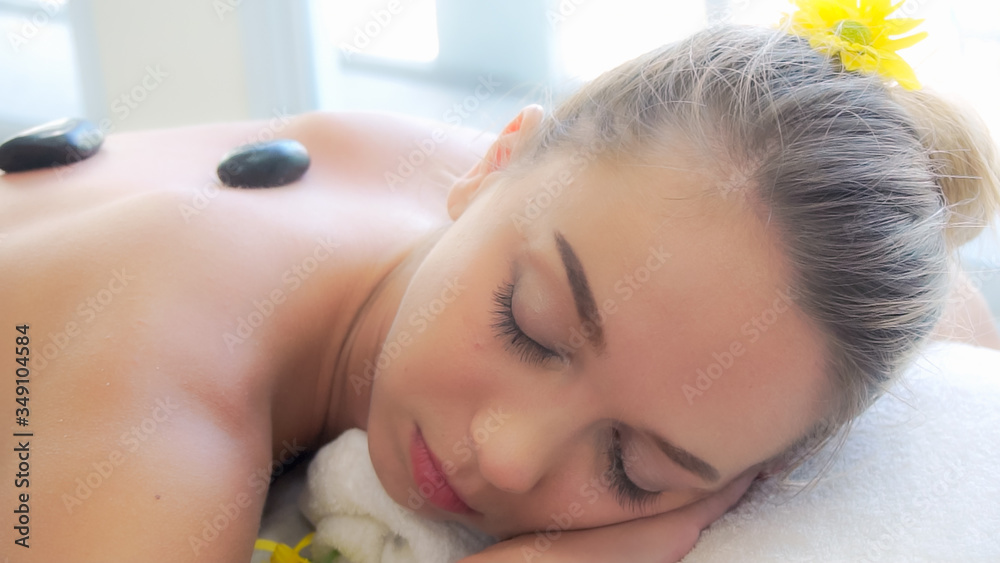 Woman getting hot stone massage treatment by professional beautician therapist in spa salon. Luxury 