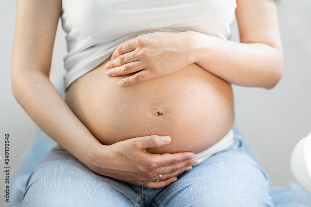 Pregnant woman hugging her belly, sitting on a gynecological chair during a medical examination, cro