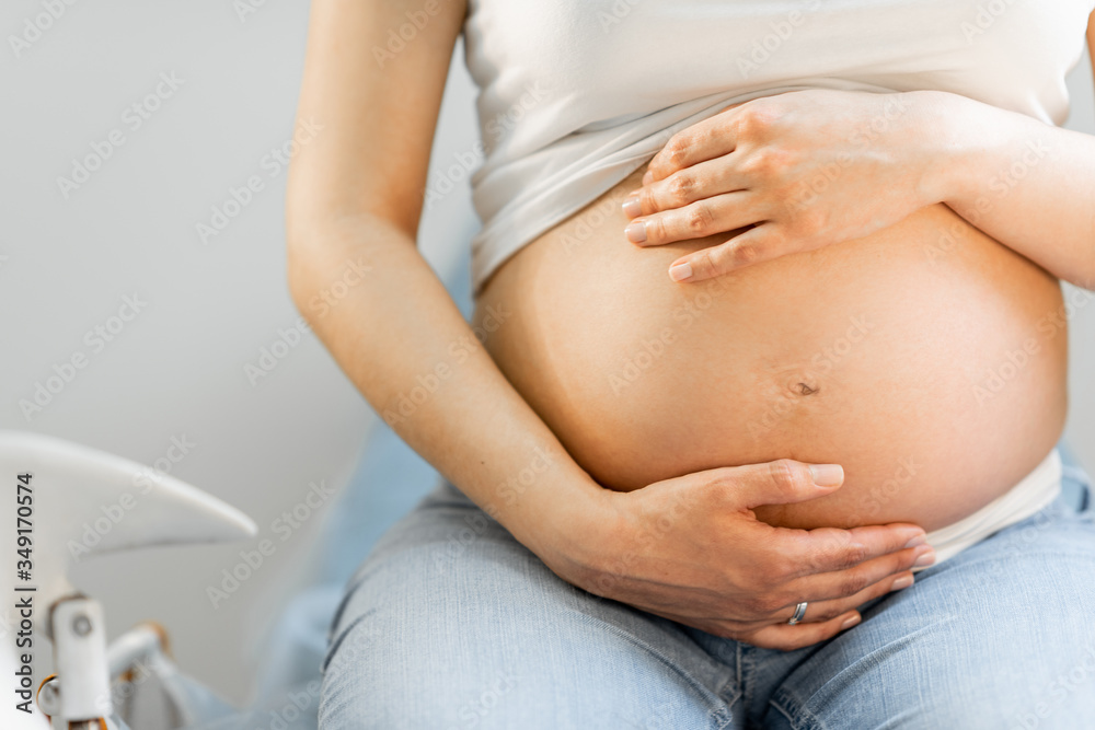 Pregnant woman hugging her belly, sitting on a gynecological chair during a medical examination, cro