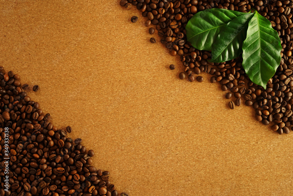 Coffee beans on brown cork background. Fresh green coffee leaves. Frame of brown coffee beans. Space