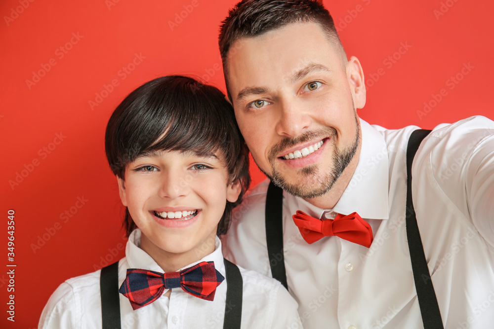 Stylish father and little son taking selfie on color background