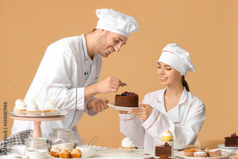 Young confectioners cooking tasty dessert on color background