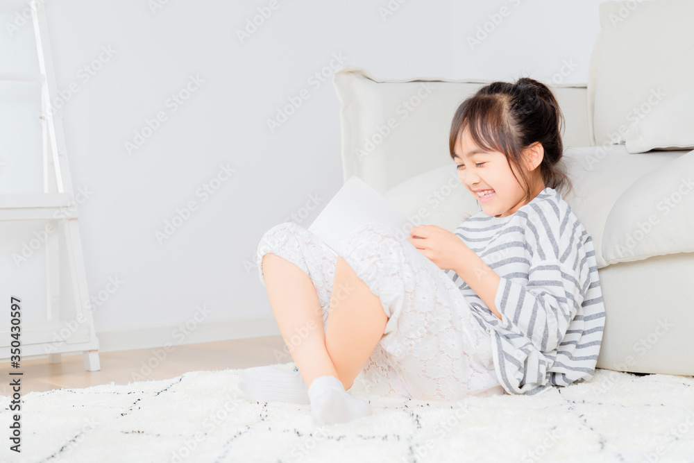 Asian little girl sitting on the carpet reading a book