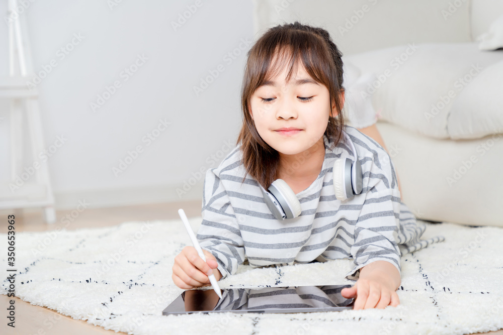 Asian little girl playing tablet on the carpet