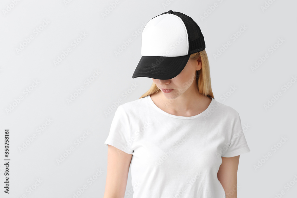 Beautiful young woman in stylish cap on light background