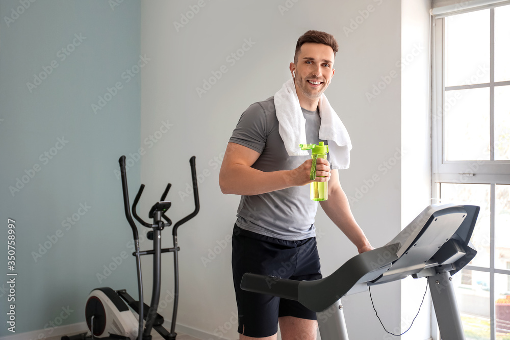 Young man drinking water after training in gym