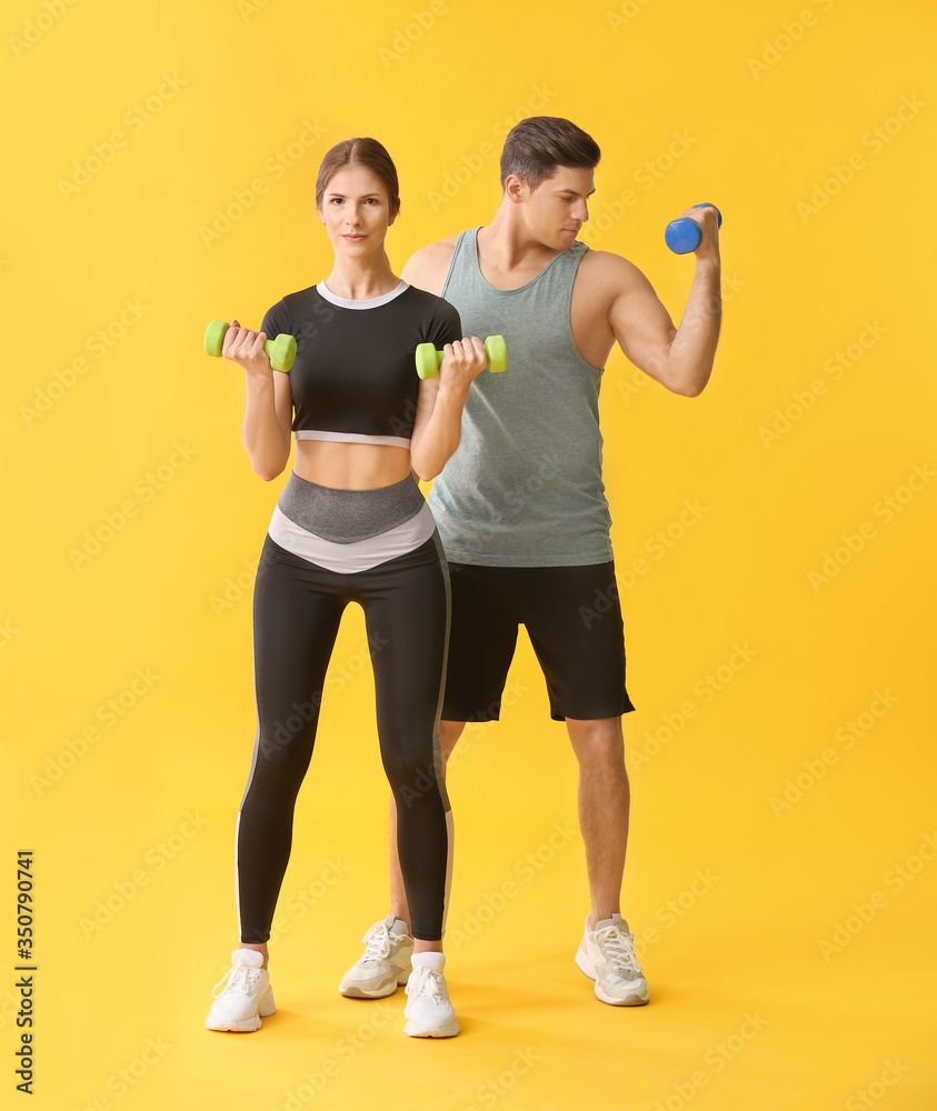 Sporty young couple with dumbbells on color background