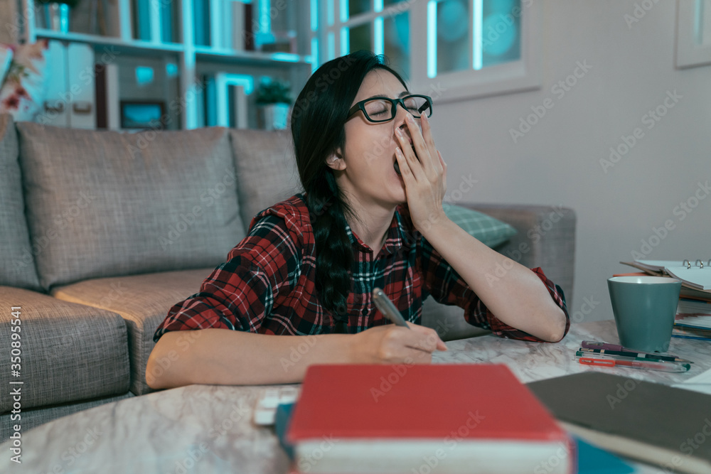 side view japanese girl studying until wee hours feels sleepy and can't stop yawning. asian 12th gra