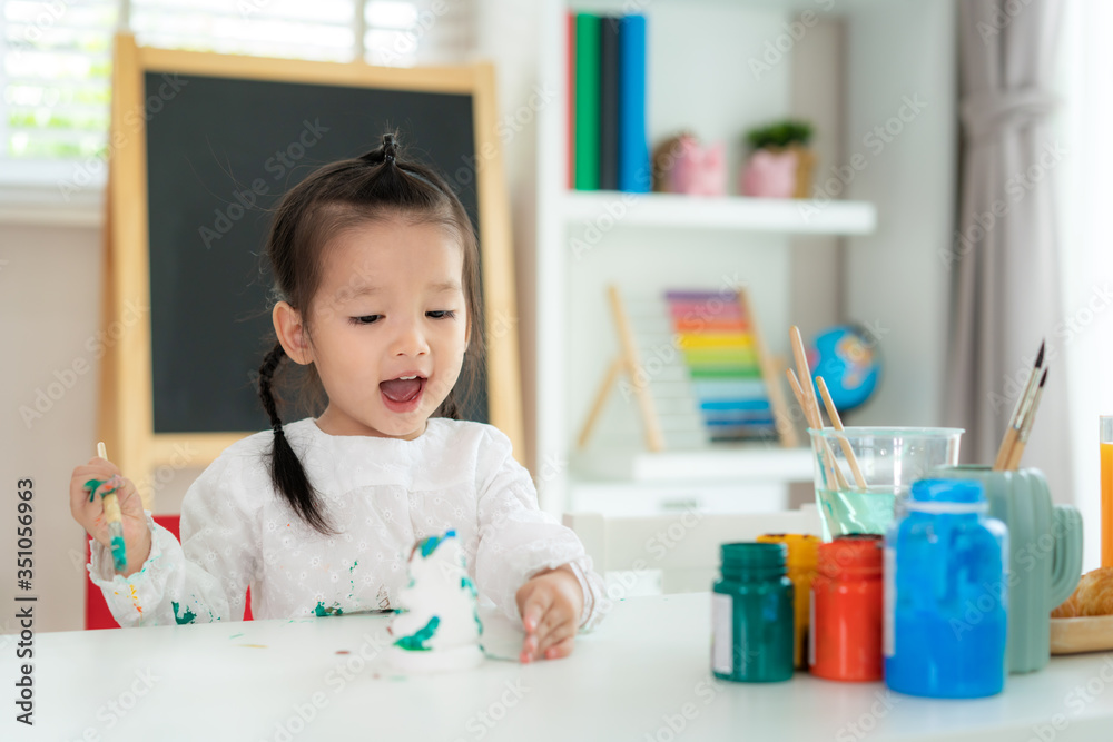 亚洲幼儿园女孩在用亚克力水画石膏娃娃时看起来很开心，面带微笑