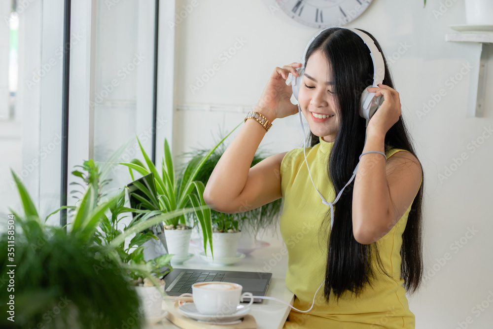 亚洲微笑女生戴无线耳机在咖啡店与skype老师在线学习，